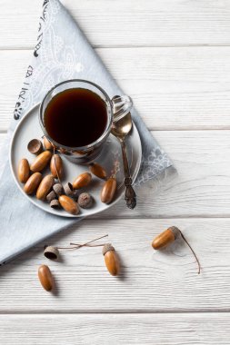 Peçeteli bir bardaktaki meşe palamudundan yapılan sıcak kahve, kahve aromalı, bol renkli ve hoş aromalı tonik bir içecektir. Beyaz ahşap arka planda