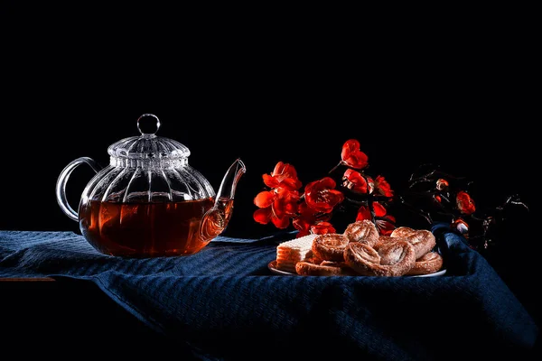 Chá quente em um bule de chá de vidro em um fundo preto. pires com biscoitos — Fotografia de Stock