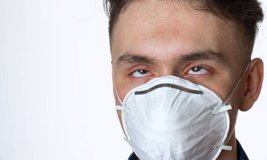 Virüs hastası, koruyucu bir maskeyle kendini izole eden genç bir adam. Kendisini ve diğerlerini koronavirüsün yayılımından korur, beyaz bir arka planda.