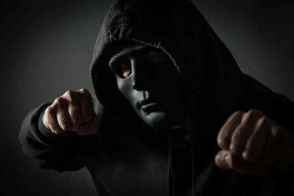 Studio shot of unrecognizable hooded man with black mask and clenched fists