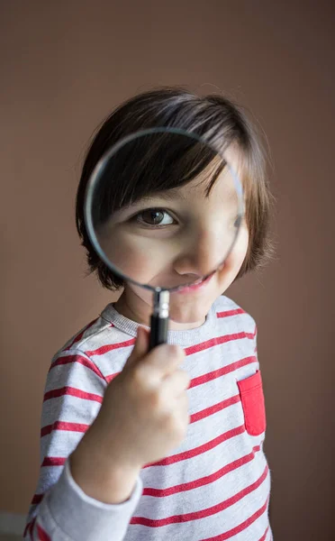 Child with magnifying glass looking at the camera with big eye