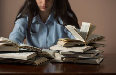 Masada oturan genç bir kız evde bir sürü kitap okuyor.