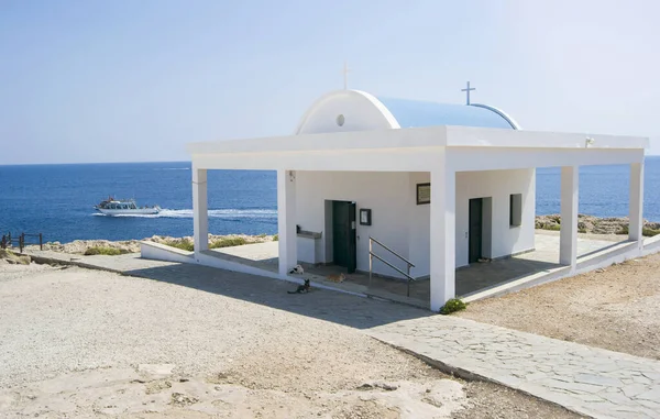 Güneşli bir günde Cape Cavo Greco 'daki Agioi Anargyroi Kilisesi. Kediler gölgede uyuyor. Denizde sürat teknesi