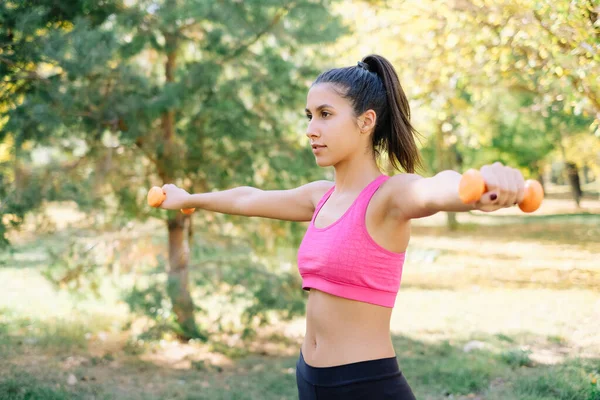 Fille travaillant avec des haltères orange dans la nature — Photo