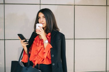 Cep telefonu kullanan ve elinde çanta tutan bir kadın.