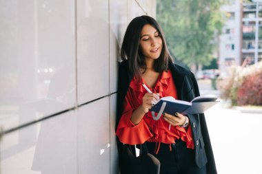 Duvara yaslanan ve kitaba yazan kız