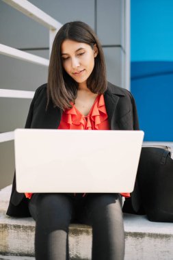 Genç bir kadın dışarıda beyaz laptopunu kullanıyor.