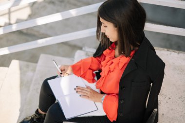 Defterde yazan ve merdivenlerde oturan kadın.