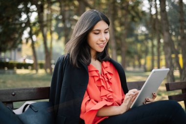 Parkta tablet kullanırken gülümseyen kız