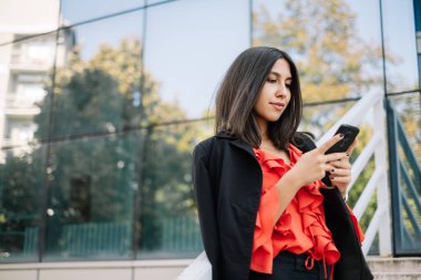 Akıllı telefonu olan bir kadın iş yerinin yakınında çalışıyor.