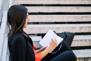 Merdivenlerde otururken deftere yazan kız.