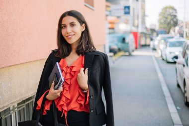 Kaldırımda dizüstü bilgisayar ve cep telefonu tutan zarif bir kız.