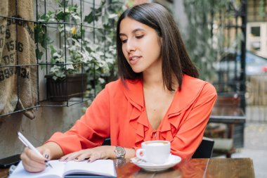 Deftere yazan ve kahve içen genç bir kadın.
