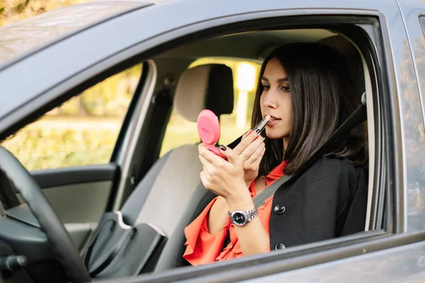 Young woman applying lipstick in the car