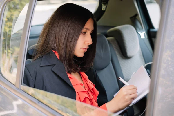 Woman writing in notebook while sitting in car — Stock Photo, Image