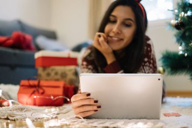 Tabletli kadın Noel ağacının yanında yatıyor.