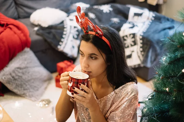 Vrouw naast kerstboom drinkend uit beker — Stockfoto