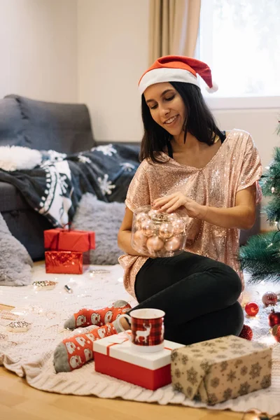 Woman with Santas hat opening box with Christmas balls