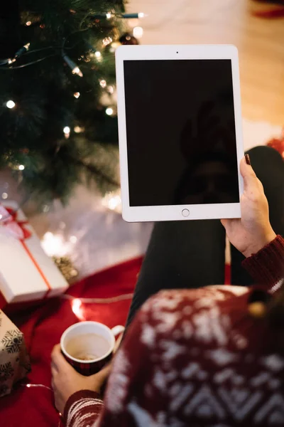 Noel ağacının yanında elinde tablet ve hediyeler tutan kadın.