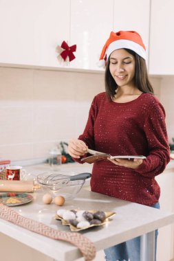 Kız mutfakta dururken kitaba bakıyor.