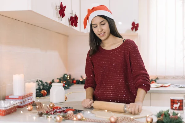 Jonge vrouw met kerstman hoed maken deeg voor koekjes — Stockfoto