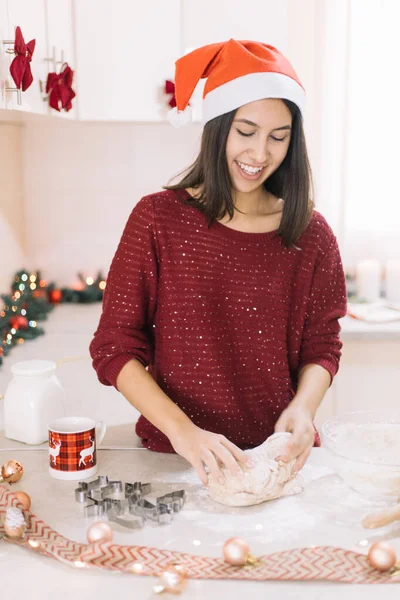 Noel Baba şapkalı gülümseyen kadın zencefilli ekmek hamuru yoğuruyor.