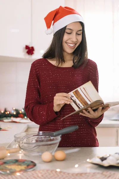 Smiling woman in kitchen reading recipe book
