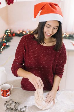 Noel Baba şapkalı gülümseyen bayan zencefilli kurabiye yapıyor.