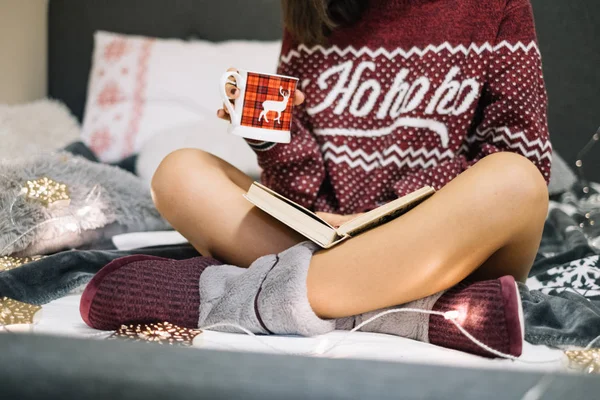 Avslappnad flicka sitter i sängen med korsade ben, medan du läser en bok — Stockfoto