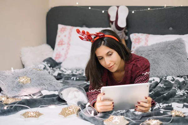 Girl using her tablet while lying in bed