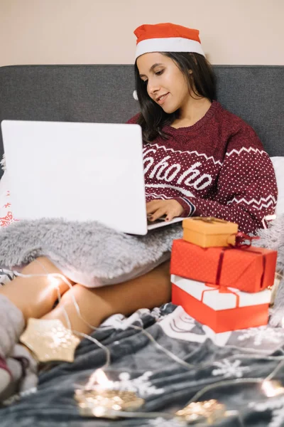 Woman laying in bed with laptop and presents