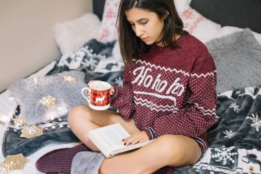 Kitap okuyan ve elinde kahve fincanı tutan bir kadın.