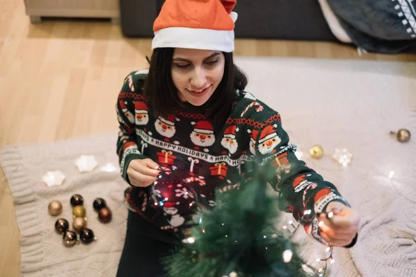 Fille habillée avec un pull de Noël décorant arbre avec des lumières — Photo