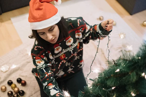 Jeune femme enveloppant arbre avec des lumières de Noël — Photo