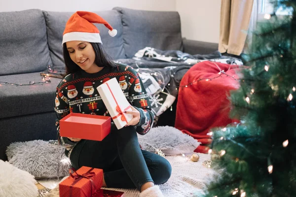 Young woman opens Christmas present near tree