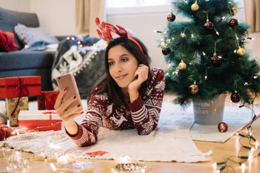 Noel ağacı ve hediyelerin yanında selfie çeken bir kadın.
