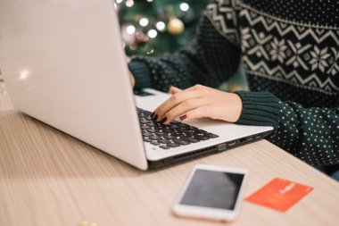 Bir kadının elleri telefon ve kartın yanında dizüstü bilgisayarda yazıyor.