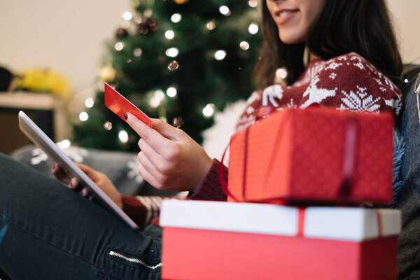 Woman holding a tablet and red card near two gift boxes