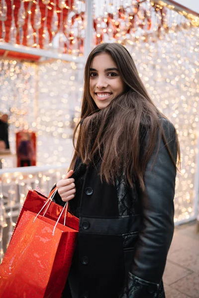 Улыбающаяся девушка с красными подарочными пакетами и огнями — стоковое фото