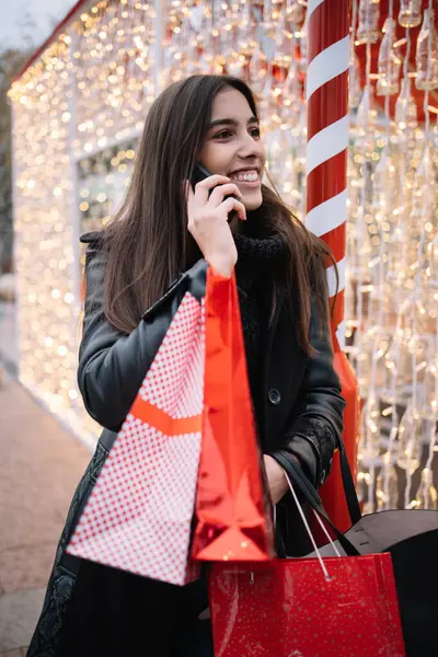 Улыбающаяся девушка с сумками возле здания со светом — стоковое фото