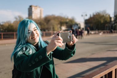 Mavi saçlı ve telefonlu bir kadının arkasından görüntü