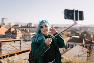 Genç bir kadın boynuna dokunuyor ve dışarıda selfie çekiyor.