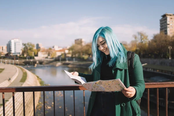 Pretty girl holding map while standing on city bridge