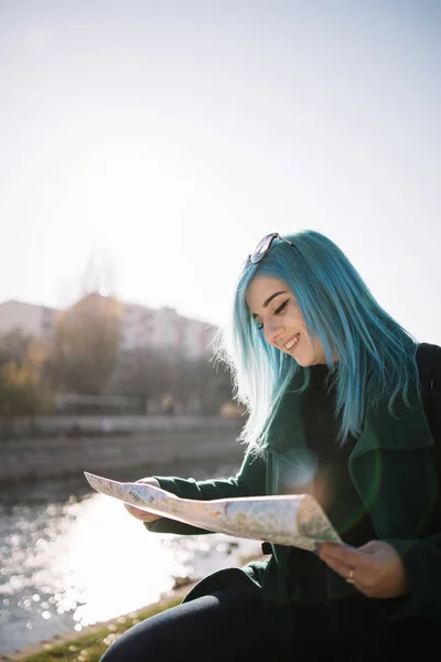 Dziewczyna z niebieskimi włosami patrząc na otwartą mapę w pobliżu rzeki — Zdjęcie stockowe