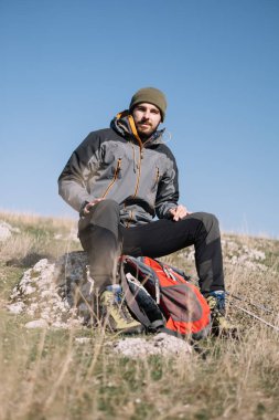 Yürüyüşçü erkek dağın tepesinde bir kayanın üzerinde oturuyor.