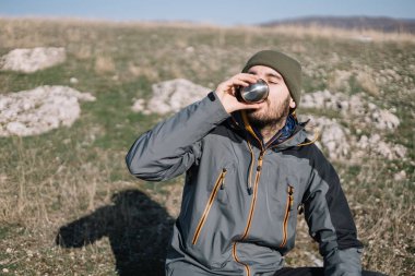 Turist, dağ manzaralı bir tarlada çay içiyor.