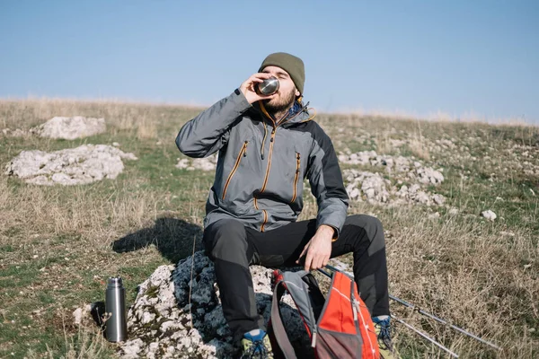 Mężczyzna turysta siedzi na skale i pije kawę — Zdjęcie stockowe