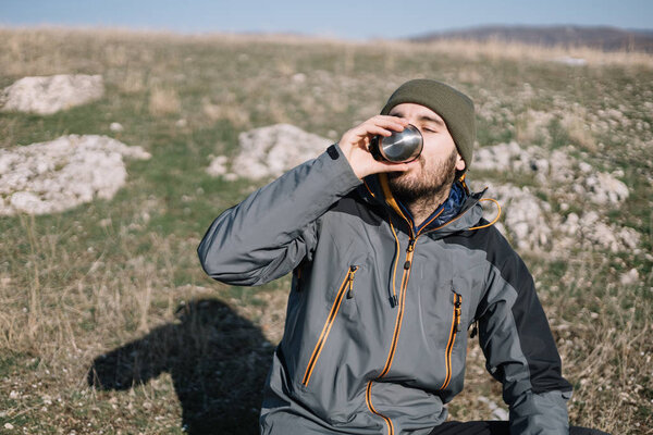 Tourist man drinking tea on a field with mountain view