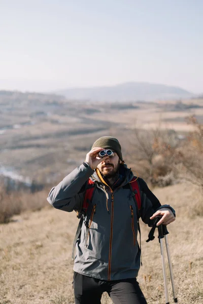 Toeristische man staat op heuvel met uitzicht op de bergen en met een verrekijker — Stockfoto