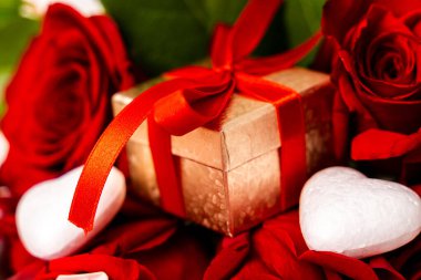 Kırmızı güller arasında kırmızı kurdeleli altın hediye kutusu